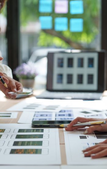 Web designers working together on a new mobile application prototype, comparing smartphone and printed layouts